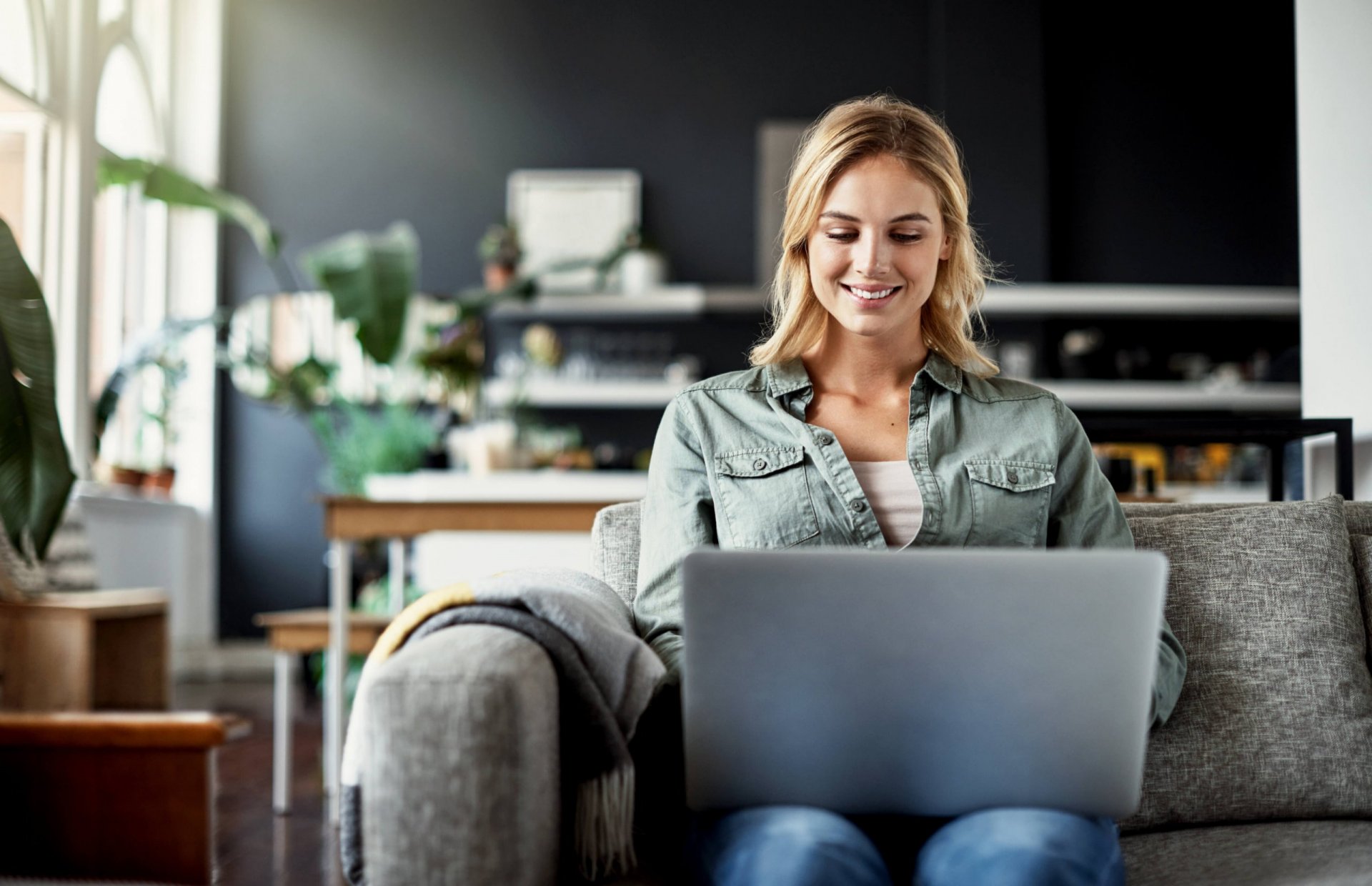 Frau sitzt auf Sofa und arbeitet am Laptop
