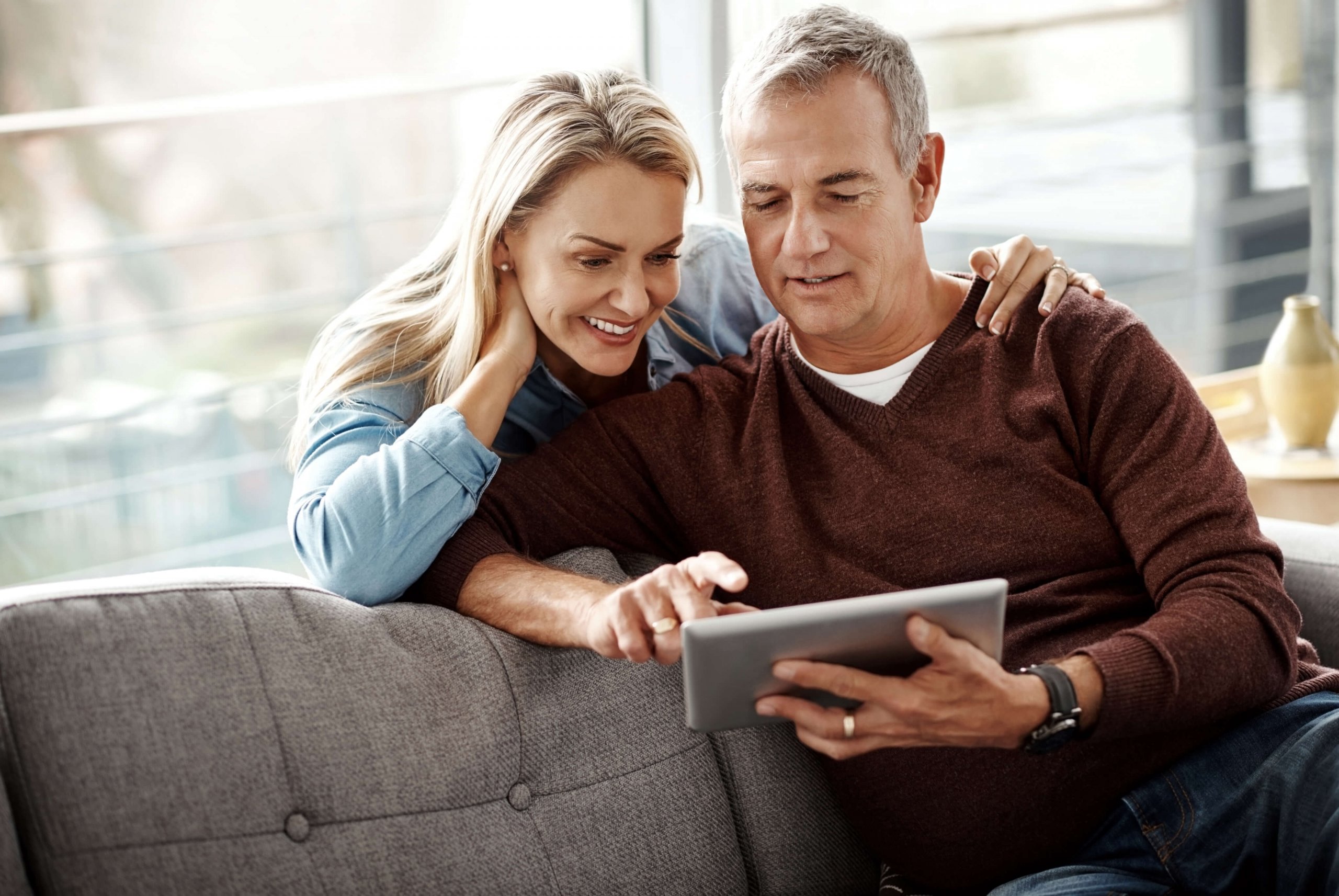 Eherpaar sitzt auf Sofa und schaut gemeinsam auf ein Tablet