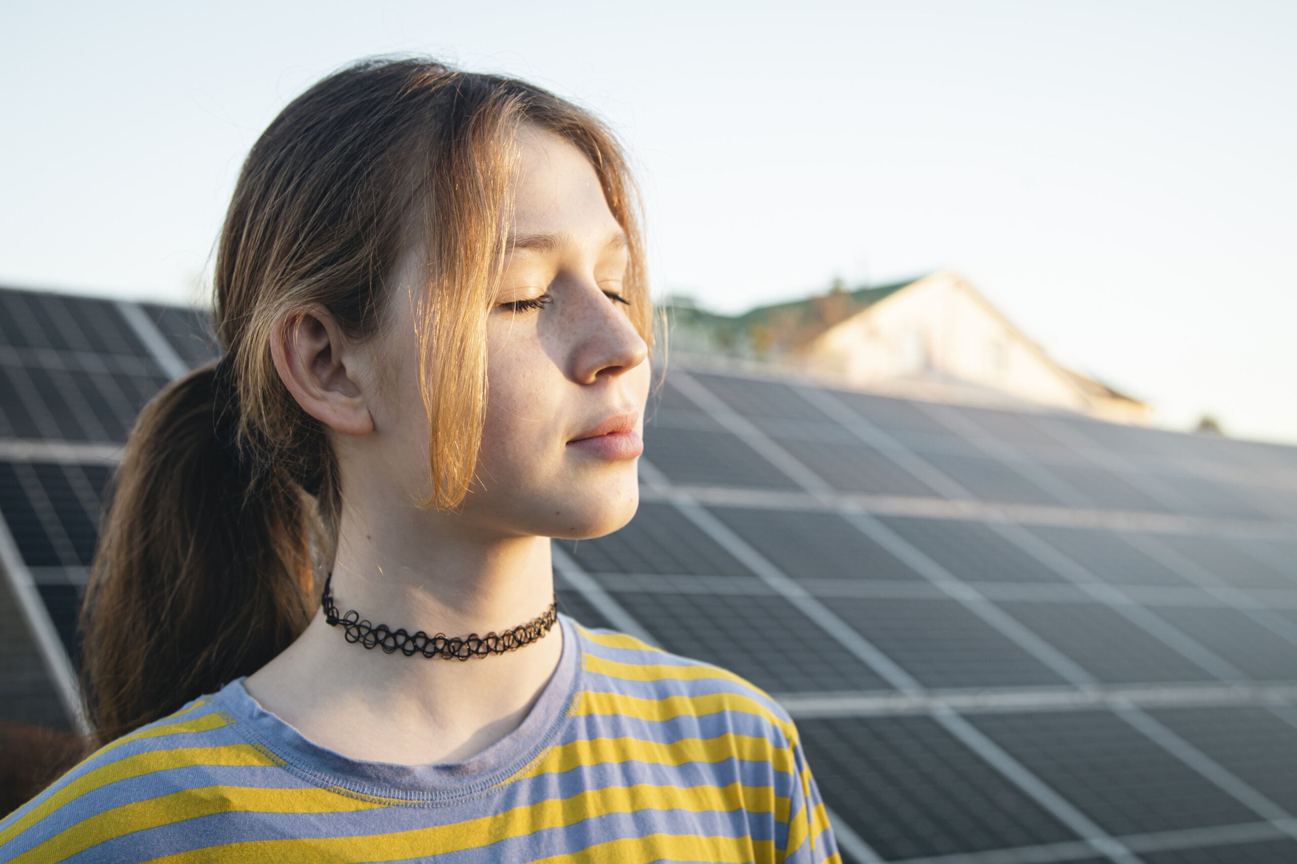 Mädchen mit geschlossenen Augen genießt die Sonne und steht vor PV-Anlage